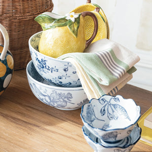 Vintage style blue and white floral designed ceramic bowls displayed on table with linen towels and coordinating cereal bowls. 