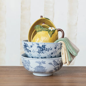 Vintage style blue and white floral designed ceramic bowls stacked on table with linens. 