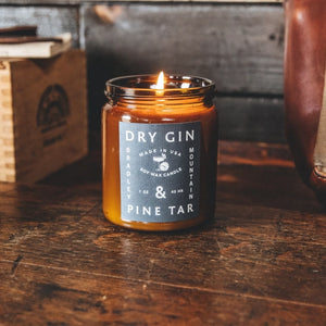 Dry gin and pine tar candle in amber glass jar with flame. 