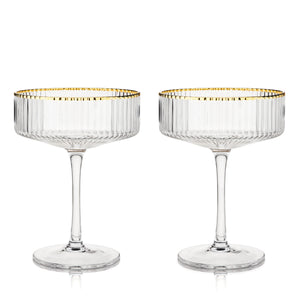 Two empty meridian fluted coupe glasses with gold rims.