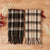 Two plaid scarves, one mostly black and the other cream, next to each other folded on a wood table.