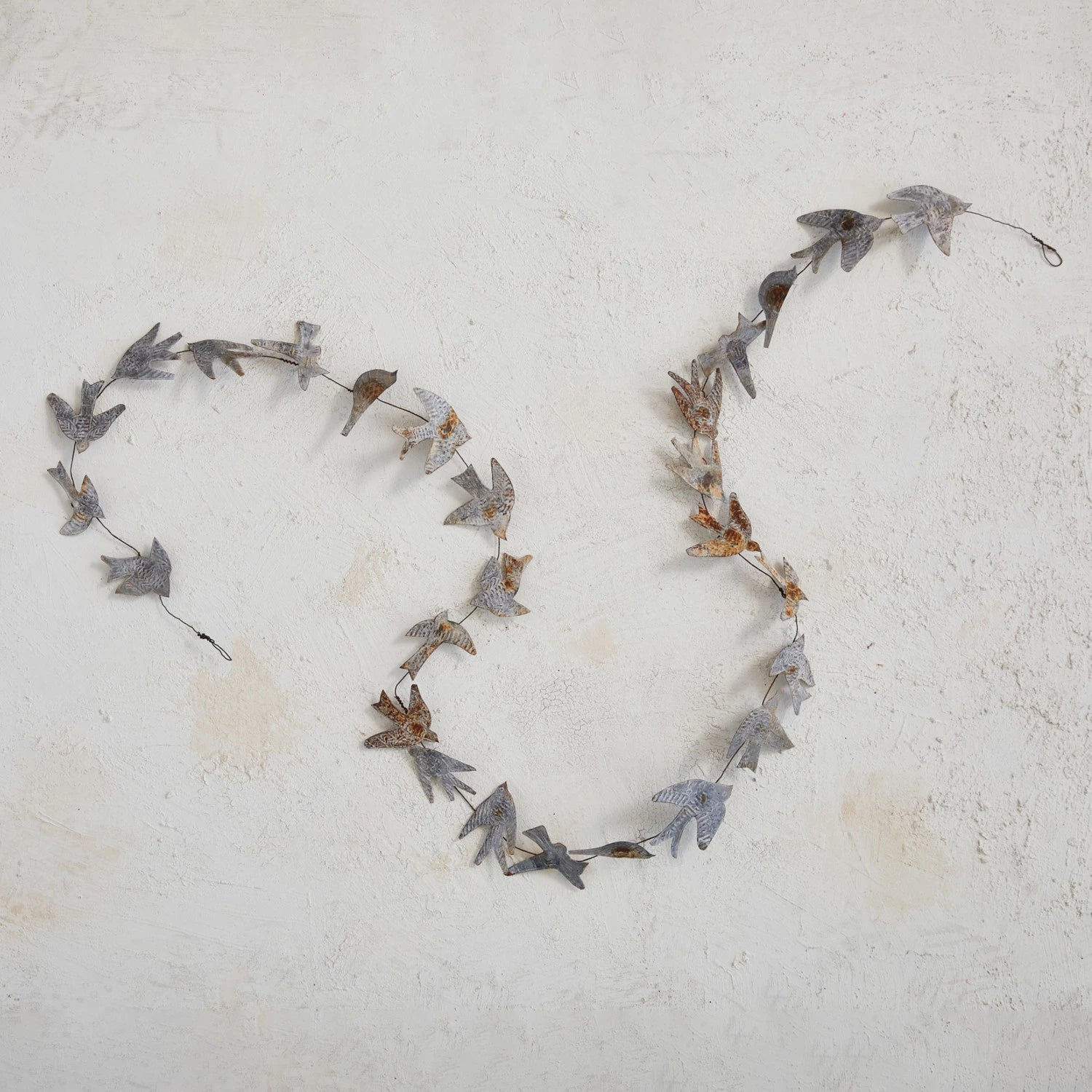 Metal and wire bird shaped rustic finished garland on a stone surface.