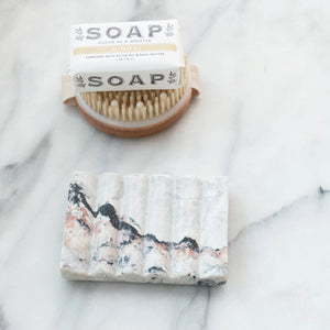 carved black and grey melange marble soap dish with bar soap and brush displayed on counter. 