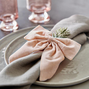 Blush pink bow napkin tie around a grey napkin with a sprig of rosemary.