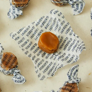 Open Jacobsen salty classic caramel on it's wrapper with other wrapped caramels surrounding it.