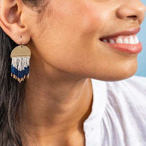 model wearing short curved brass beaded fringe earrings in navy, white, and gold. 
