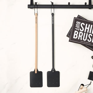 The wood and leather fly swatter hanging on a black coat rack.