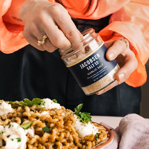 Person using Jacobsen garlic salt to season a pasta dish.