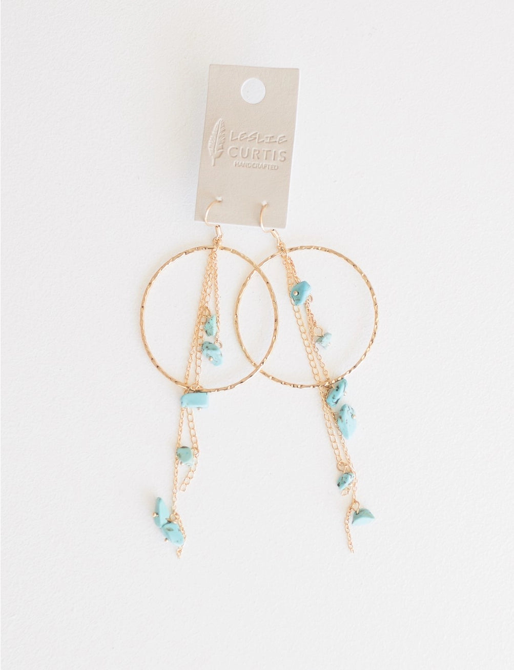 Gold hoop earrings with turquoise stones dangling inset of hoop on leather tag. Made in the USA. Leslie Curtis