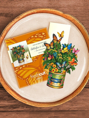 Butterfly and buttercup flower bouquet in a honey jar with the mailing envelope and blank notecard displayed on a plate.