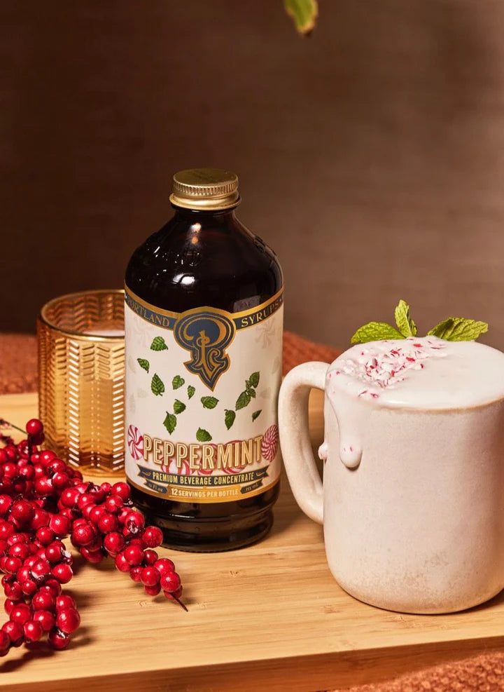 the peppermint syrup bottle next to a full hot cocoa mug and stem of cranberries.