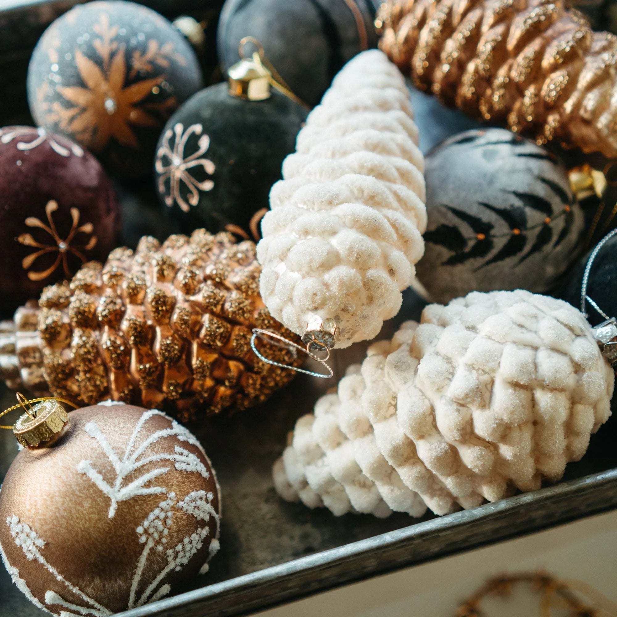 Two white pinecone ornaments on a pile of other holiday ornaments.