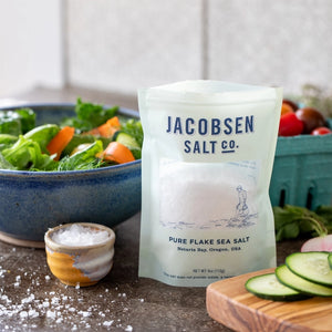 bag of Jacobsen pure flake sea salt next to salad and fresh cut vegetables.