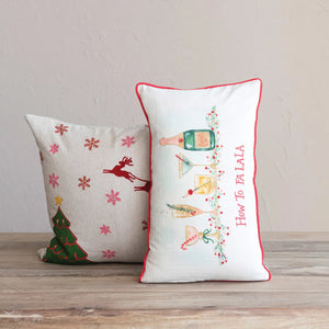 "How to Fa La La" lumbar pillow sitting upright next to another holiday pillow on a wood table.