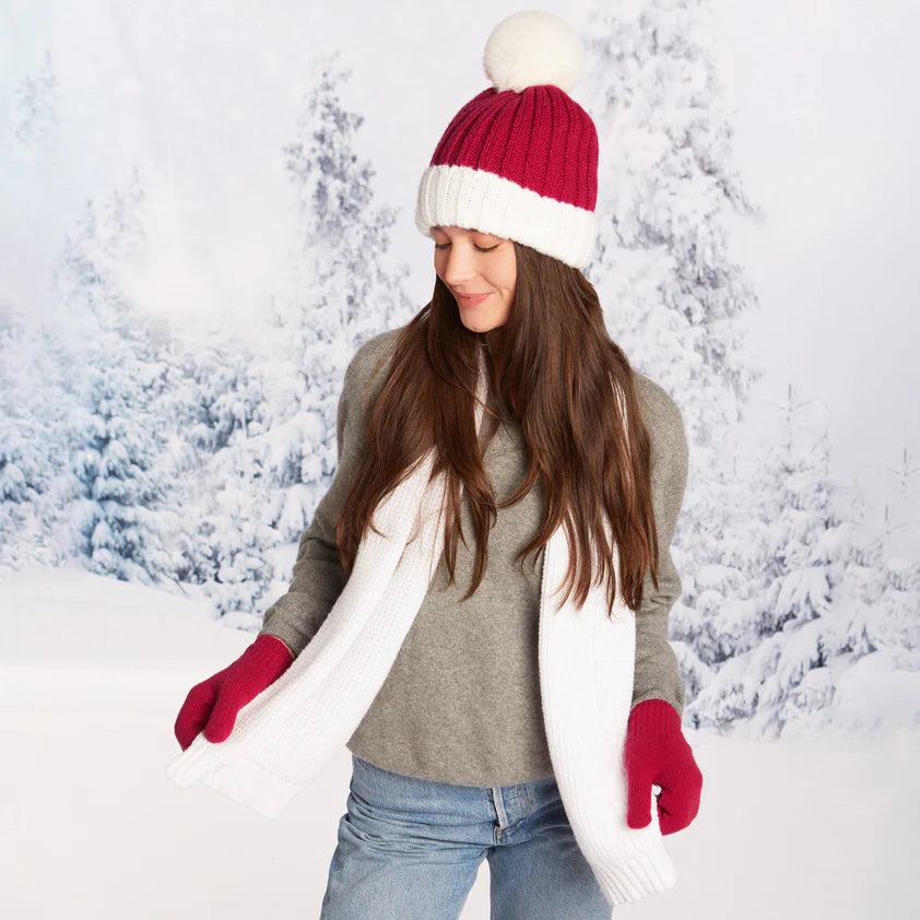 Woman wearing a red and white beanie cap and red mittens in a snowy landscape.