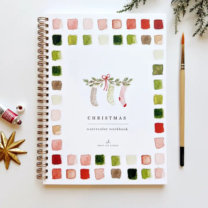 Front of Christmas Watercolor Workbook with color swatched around the border and spiral bound edge. There's a watercolor brush and paint next to it.