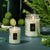 Two glass jar candles on a blue table with greenery.