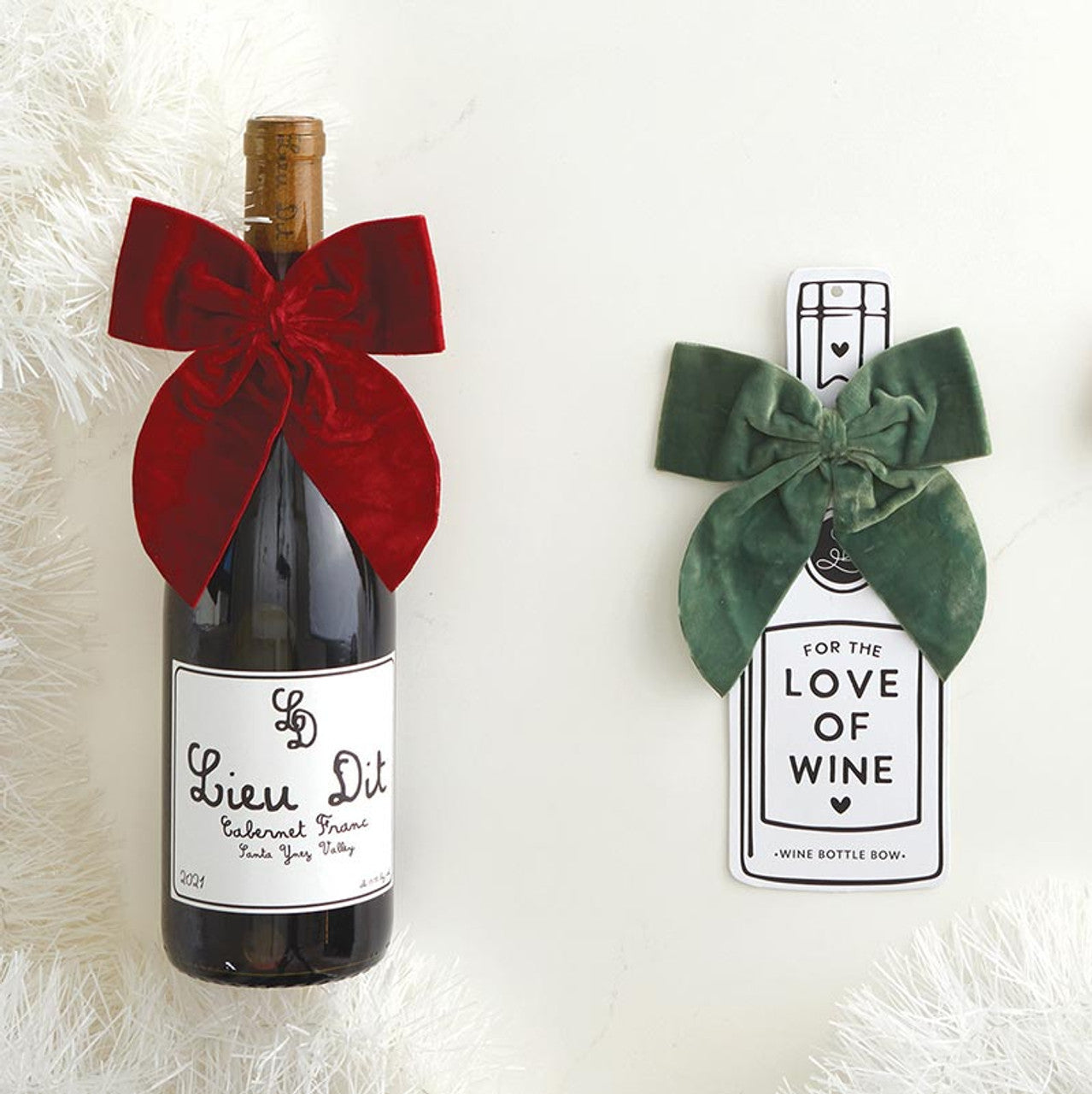 Wine bottle with a red velvet bow next to a cardboard display with a green wine bottle bow.